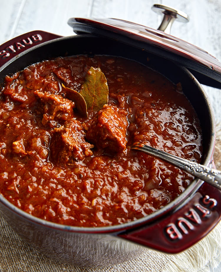 Close up view of German Goulash in a burgundy pot with a spoon inside.