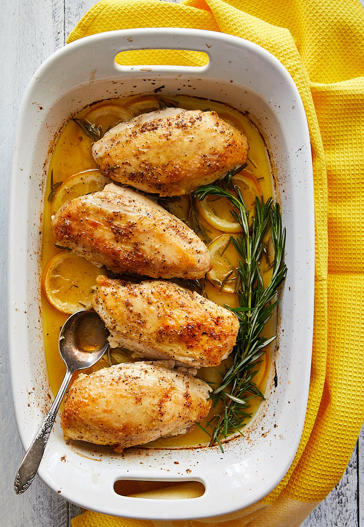 Rosemary and Lemon Chicken in a large white baking dish with lemon slices and rosemary twigs.