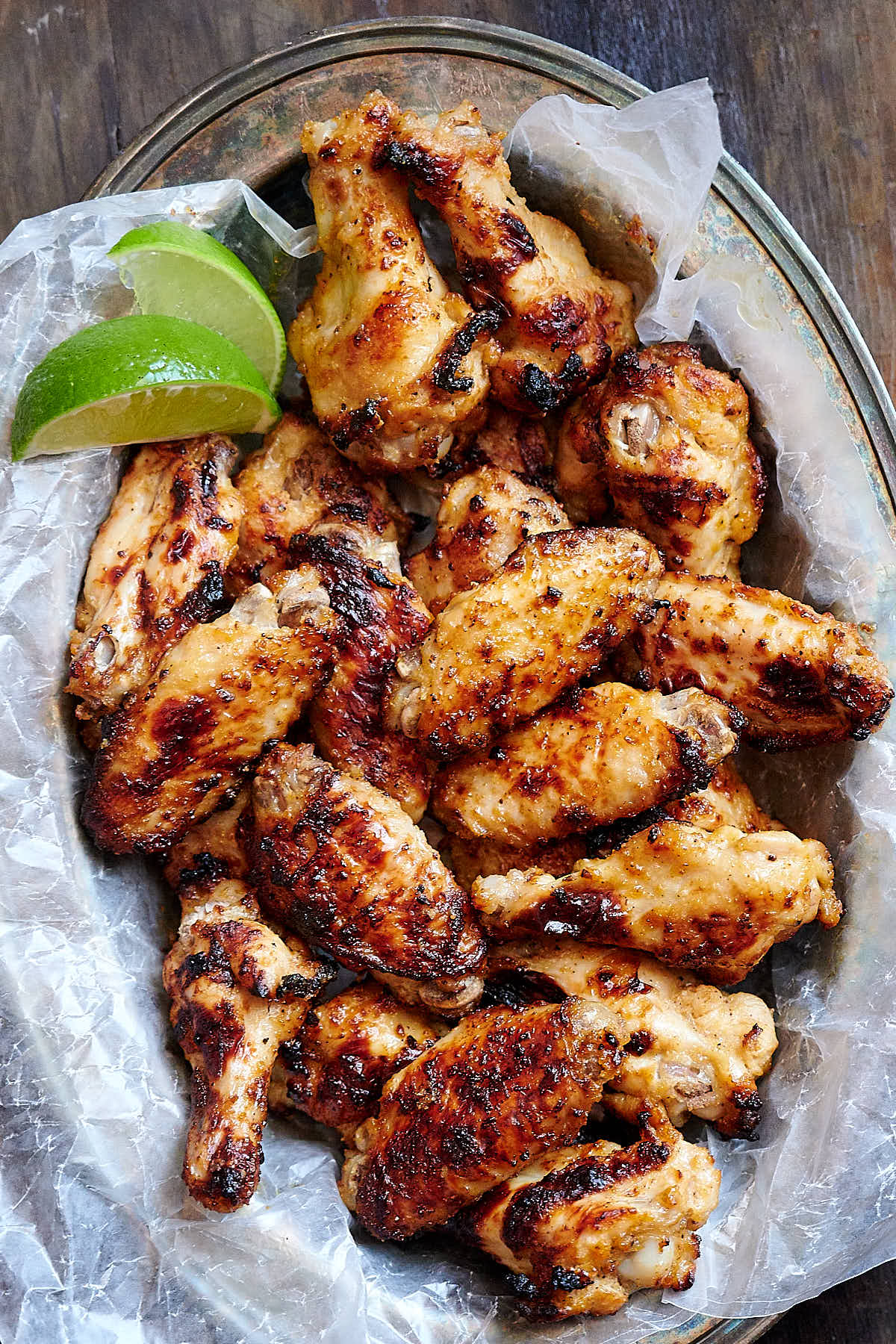 Broiled chicken wings, with lime wedges on the side, on white wax paper in a serving basket.