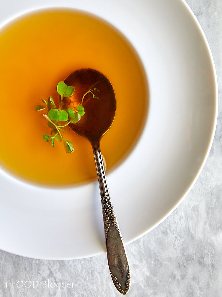 Beef Consomme in a white soup bowl with a spoon inside and garnished with micro greens.