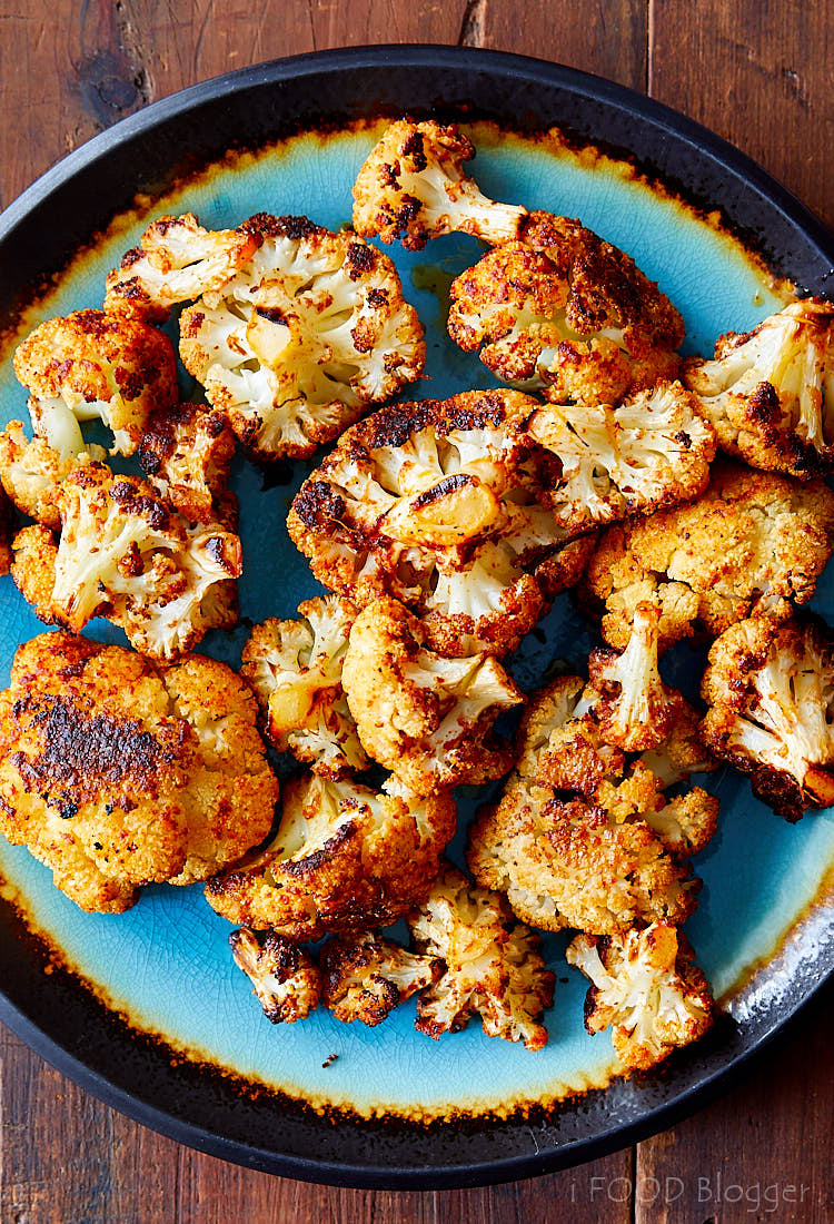 Top down view of crispy browned cauliflower pieces on a blue plate with black rim.