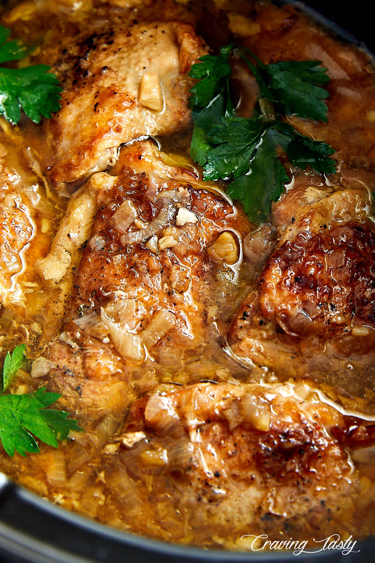 Pieces of golden brown chicken pieces in slow cooker pot, with pot juices and fresh parsley.