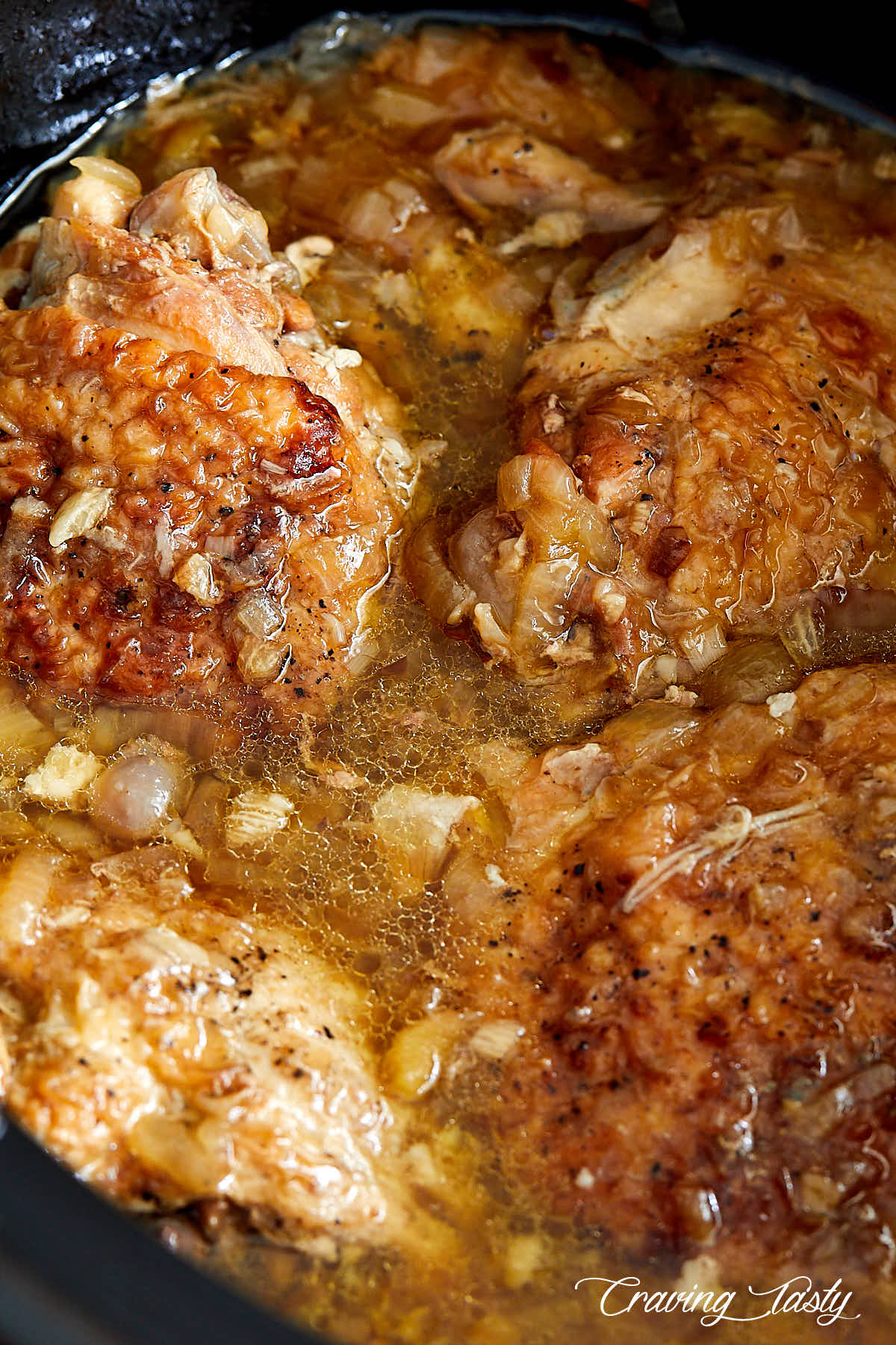 Chicken thighs inside a slow cooker, covered in juices.