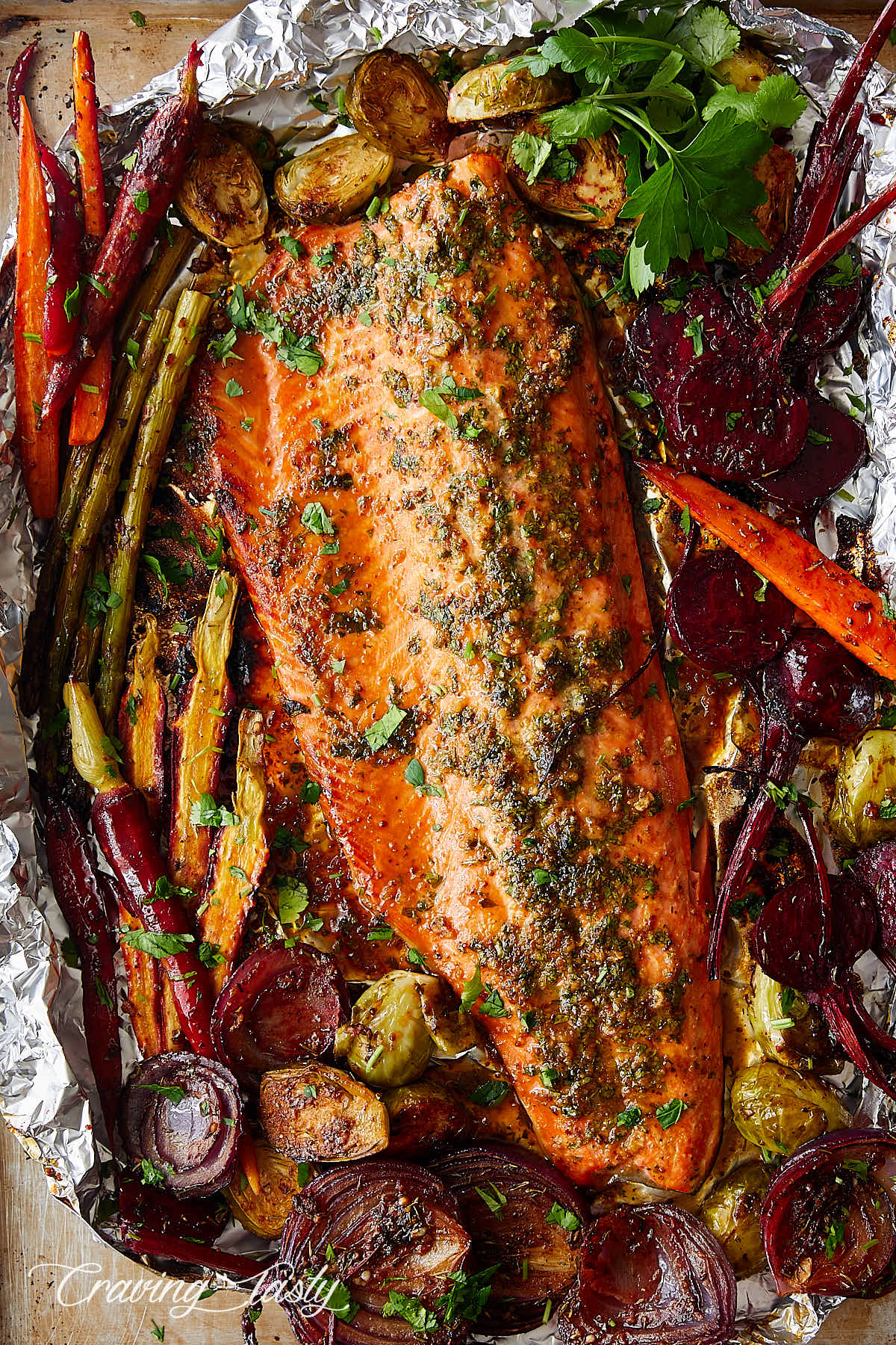Steelhead trout filet on a piece of foil surrounded by roasted vegetables.