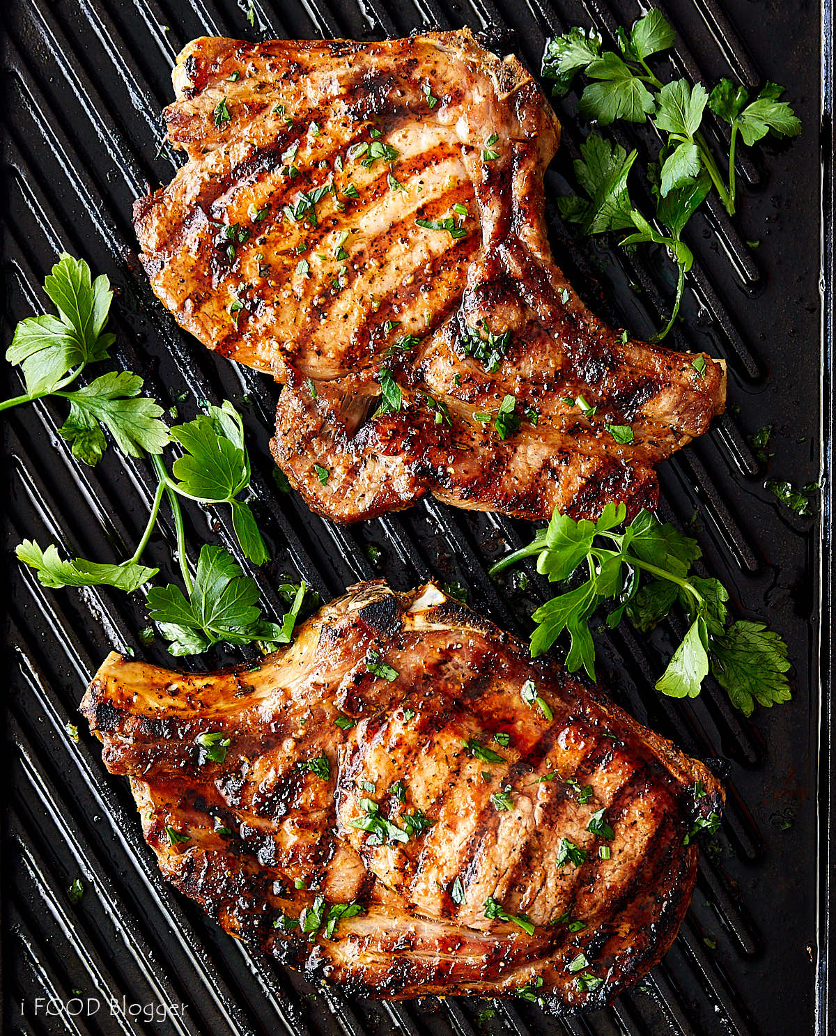 Broiled Pork Chops garnished with parsley on a ribbed black cast iron griddle.