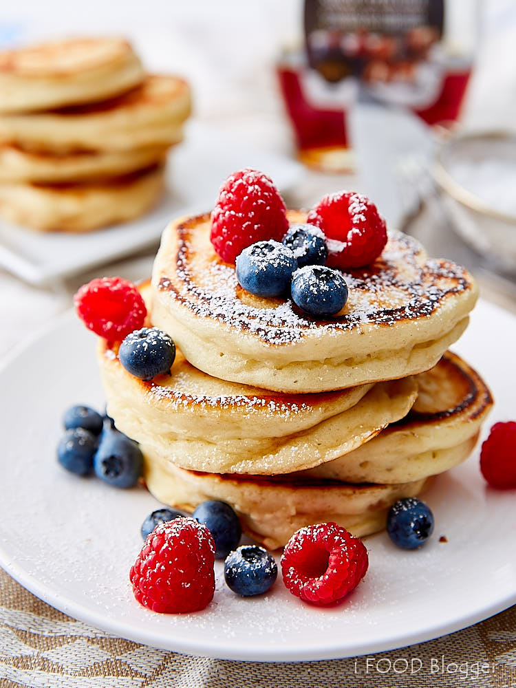 A stack of eggless pancakes on a white plate and garnished with berries and dusted with powdered sugar.