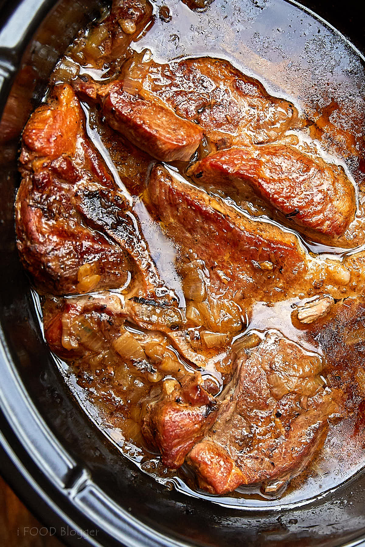 Country style pork ribs inside a slow cooker with amber color juices at the bottom, top down view.