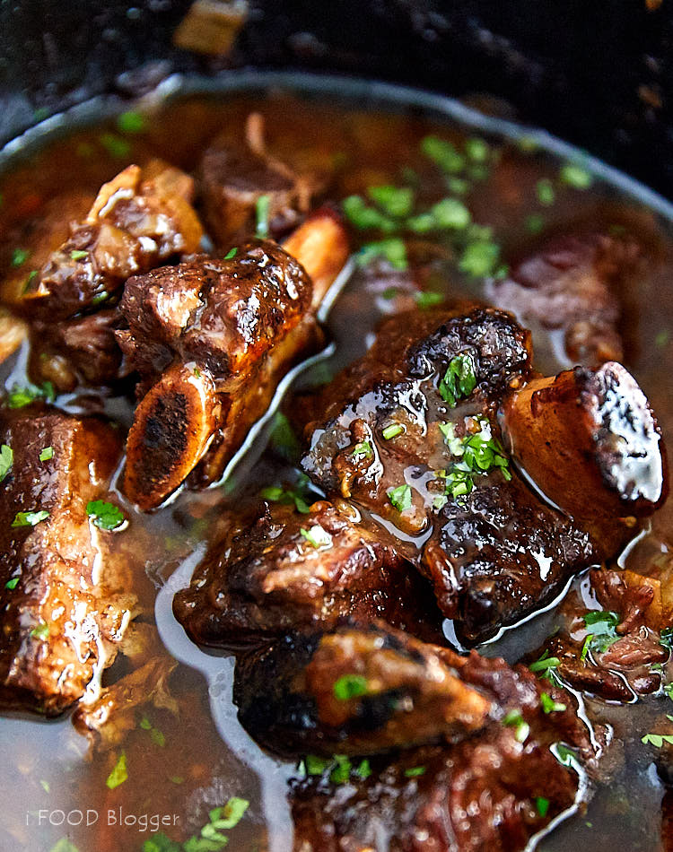 Close up of beef short ribs in a slow cooker, garnished with chopped parsley.