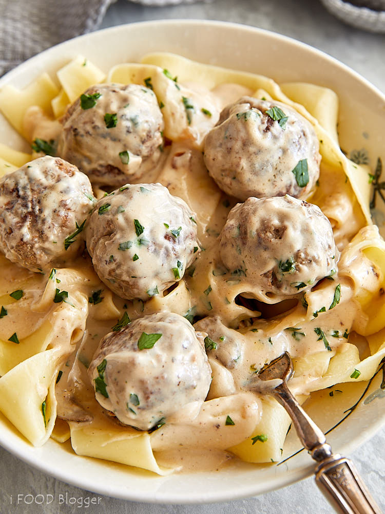 A close up of a white bowl full of Swedish meatballs with cream of mushroom sauce over pasta.