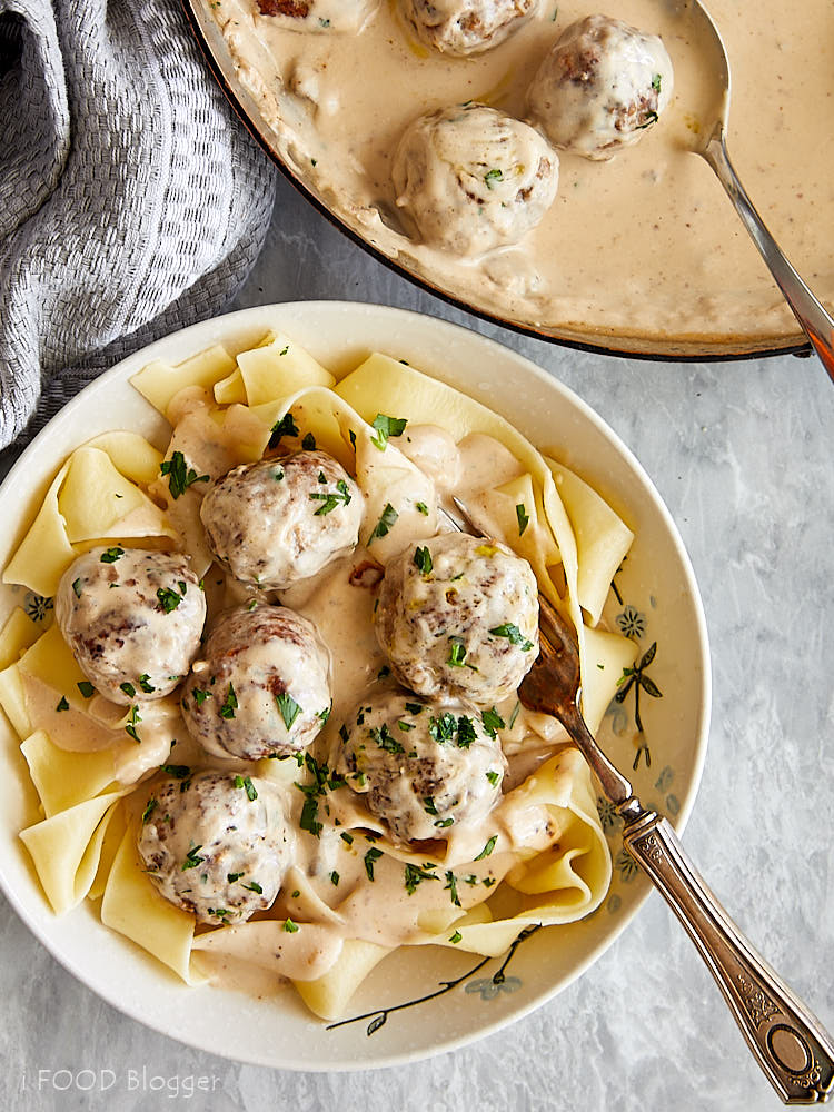A bowl of Swedish meatballs with pasta, a large pan of meatballs nearby.