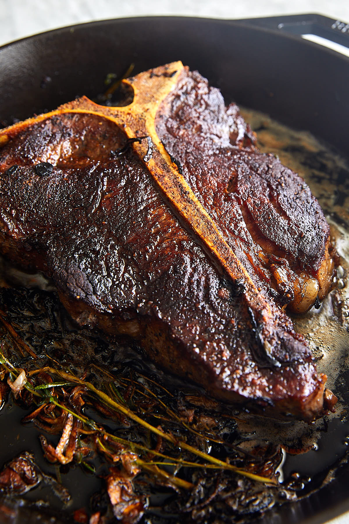 Porterhouse Steak in a cast iron pan with herbs.