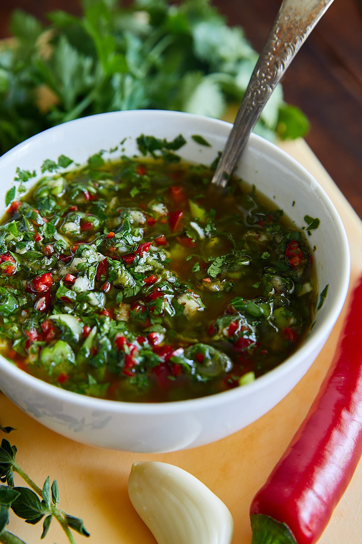 Cilantro Chimichurri in a bowl with vegetables and herbs next to it.