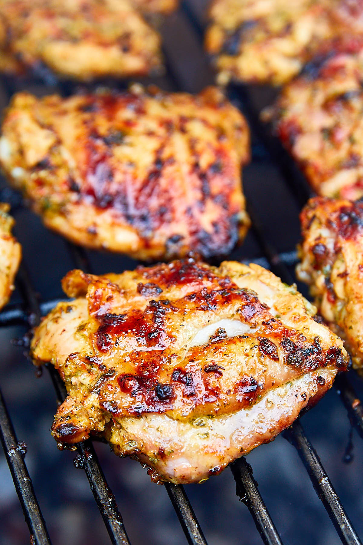 Chicken thighs on a charcoal grill rack over hot charcoal.
