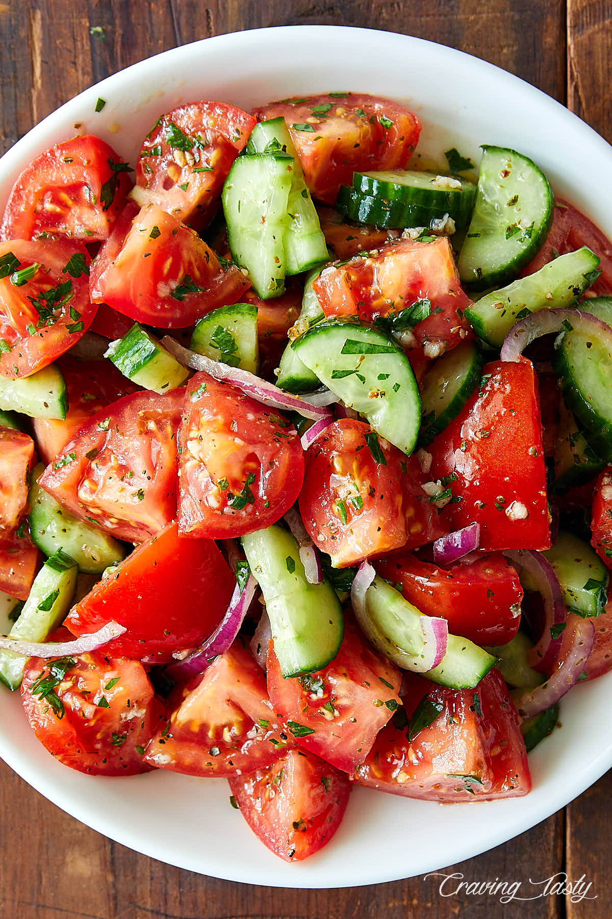 Top down view of a tomato and cucumber salad in a white bowl.