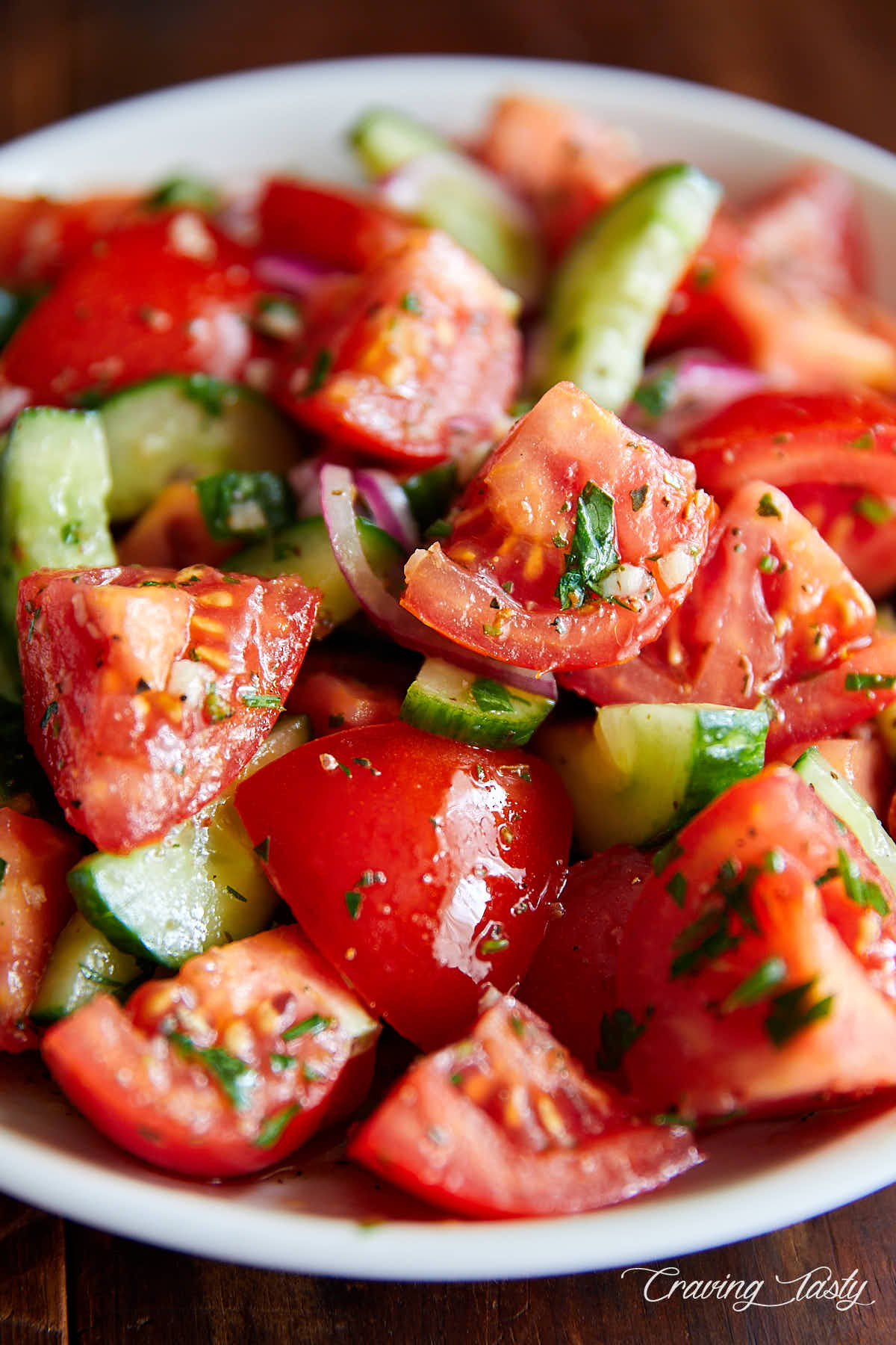 Close up of juicy, chunky tomatoes and cucumbers covered in dressing.