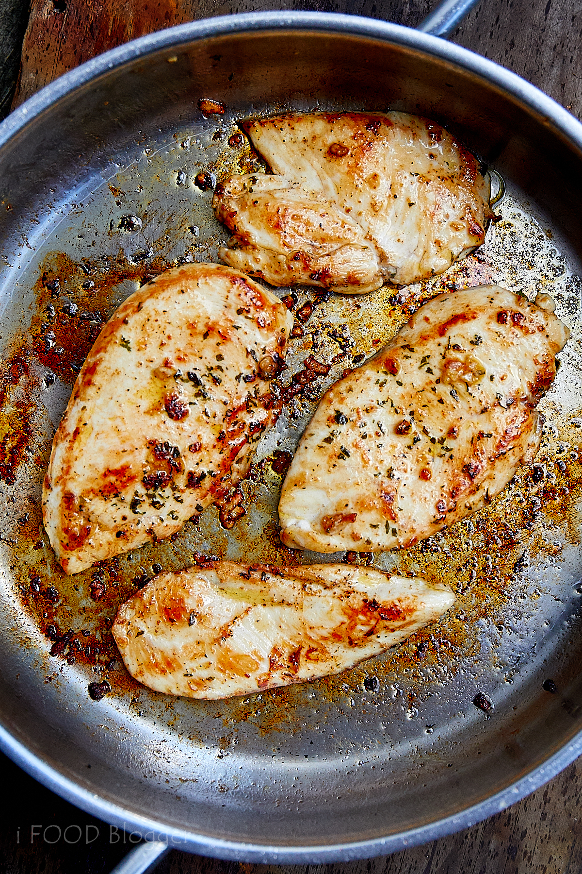 Four golden brown pan-fried chicken breasts in a stainless steel pan.