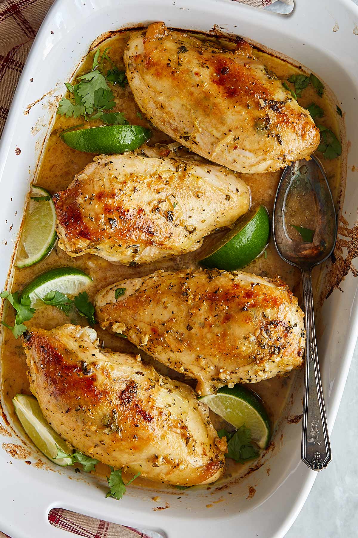 Baked chicken breasts in a white baking dish garnished with lime wedges and fresh parsley.