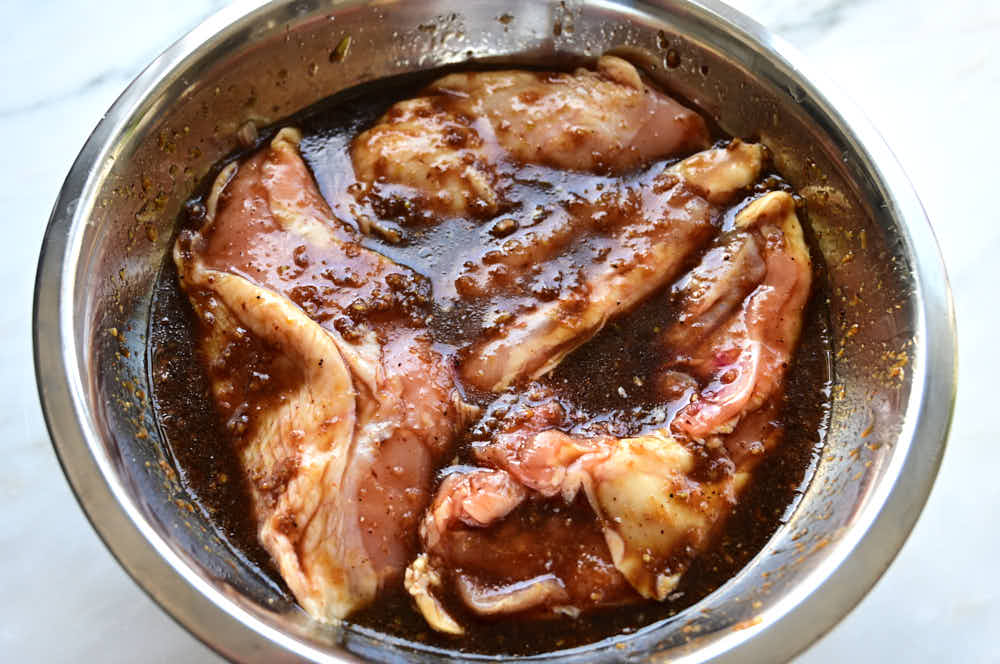 Chicken breasts in marinade in a bowl.