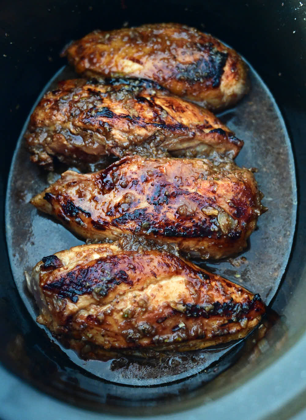 Skin-on chicken breasts inside a Crock Pot.