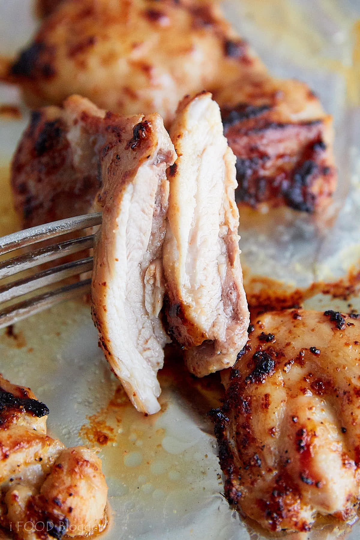 Two juicy, moist broiled chicken thigh pieces on a fork.