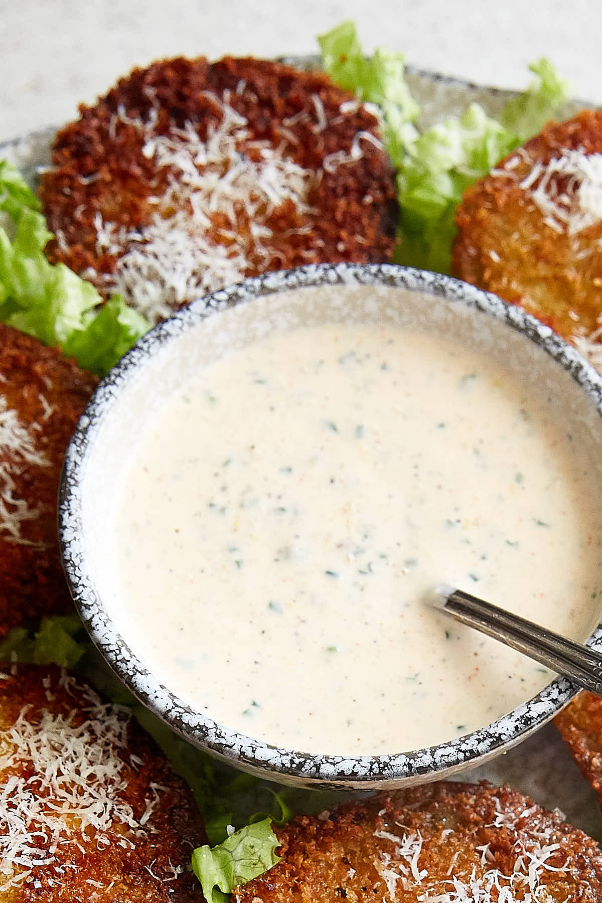 A grey speckled bowl filled with homemade buttermilk ranch dressing, with a spoon inside and fried tomatoes arranged around it.