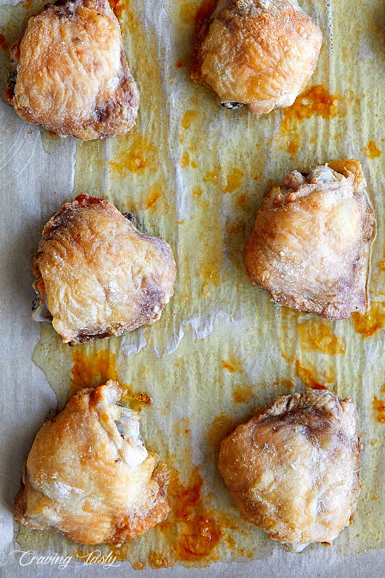 Baked chicken thighs showcasing extra crispy skin tops on a baking sheet lined with parchment paper.