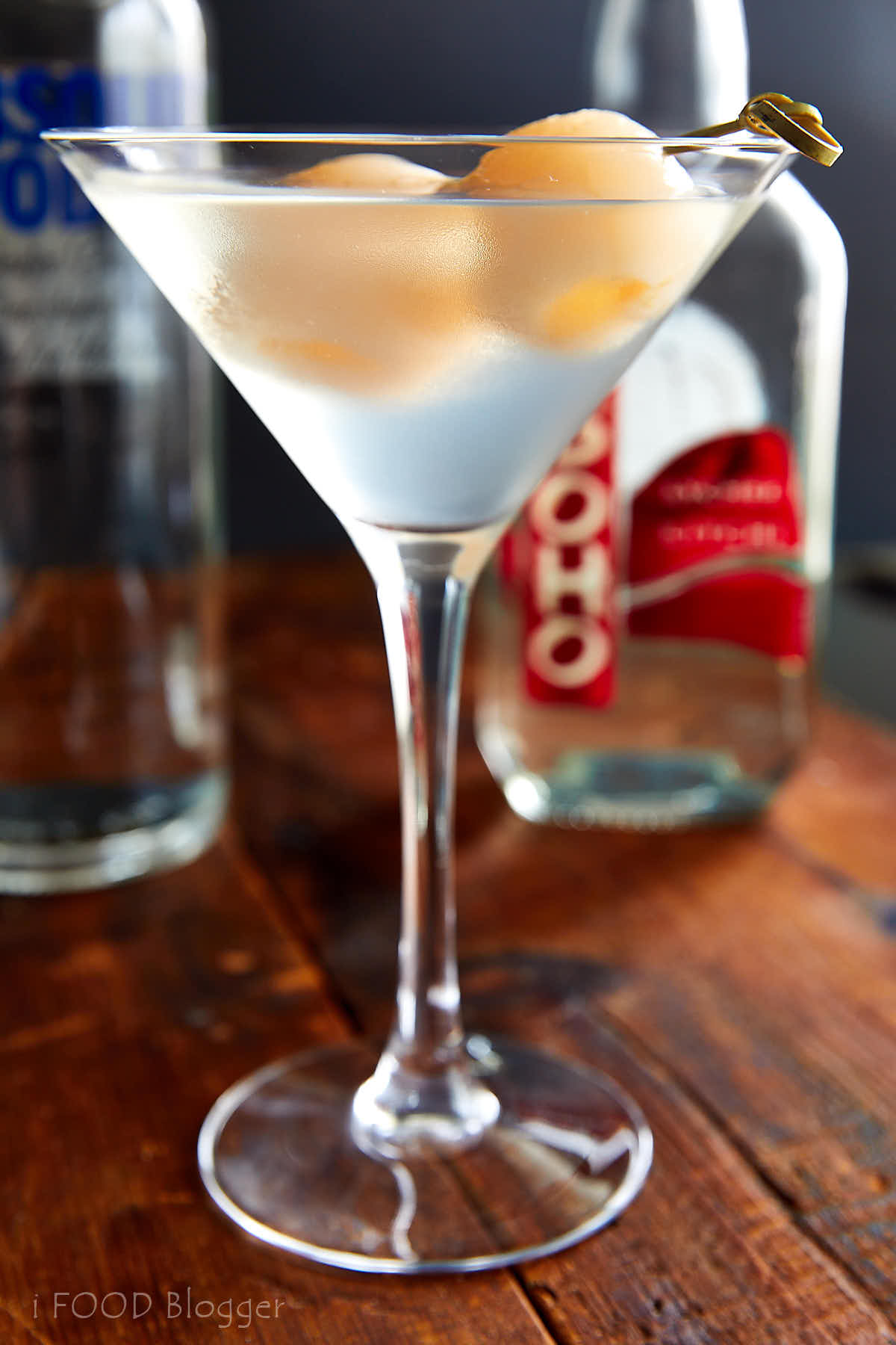 Lychee martini in a martini glass with two lychee fruit on a stick inside the glass.