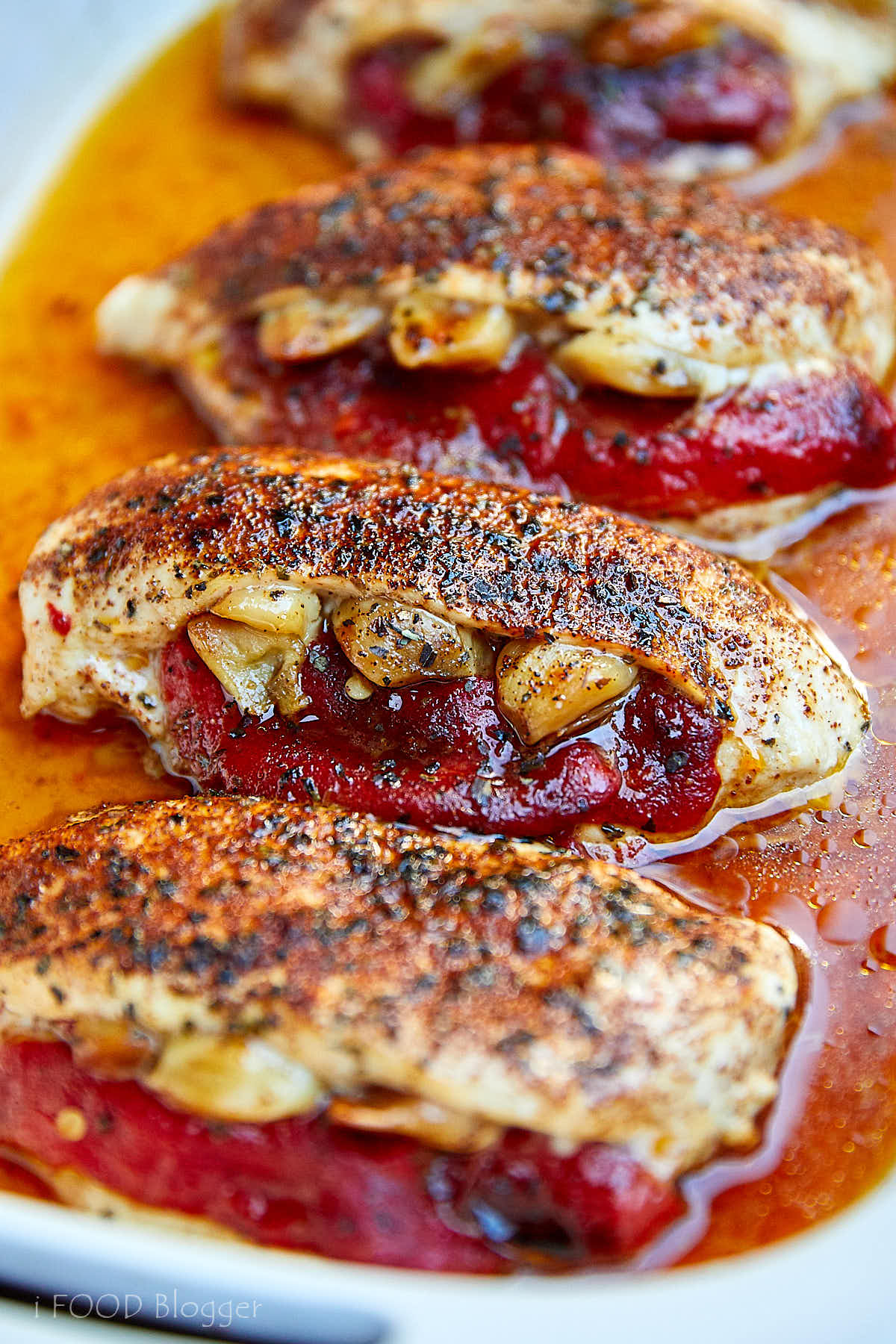 Stuffed baked chicken breasts in baking dish with pan juices on the bottom.