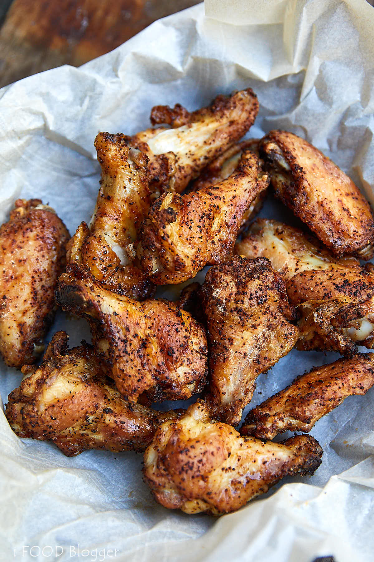 Top down view of very crispy, golden-brown chicken wings in a basket lined with wax paper.