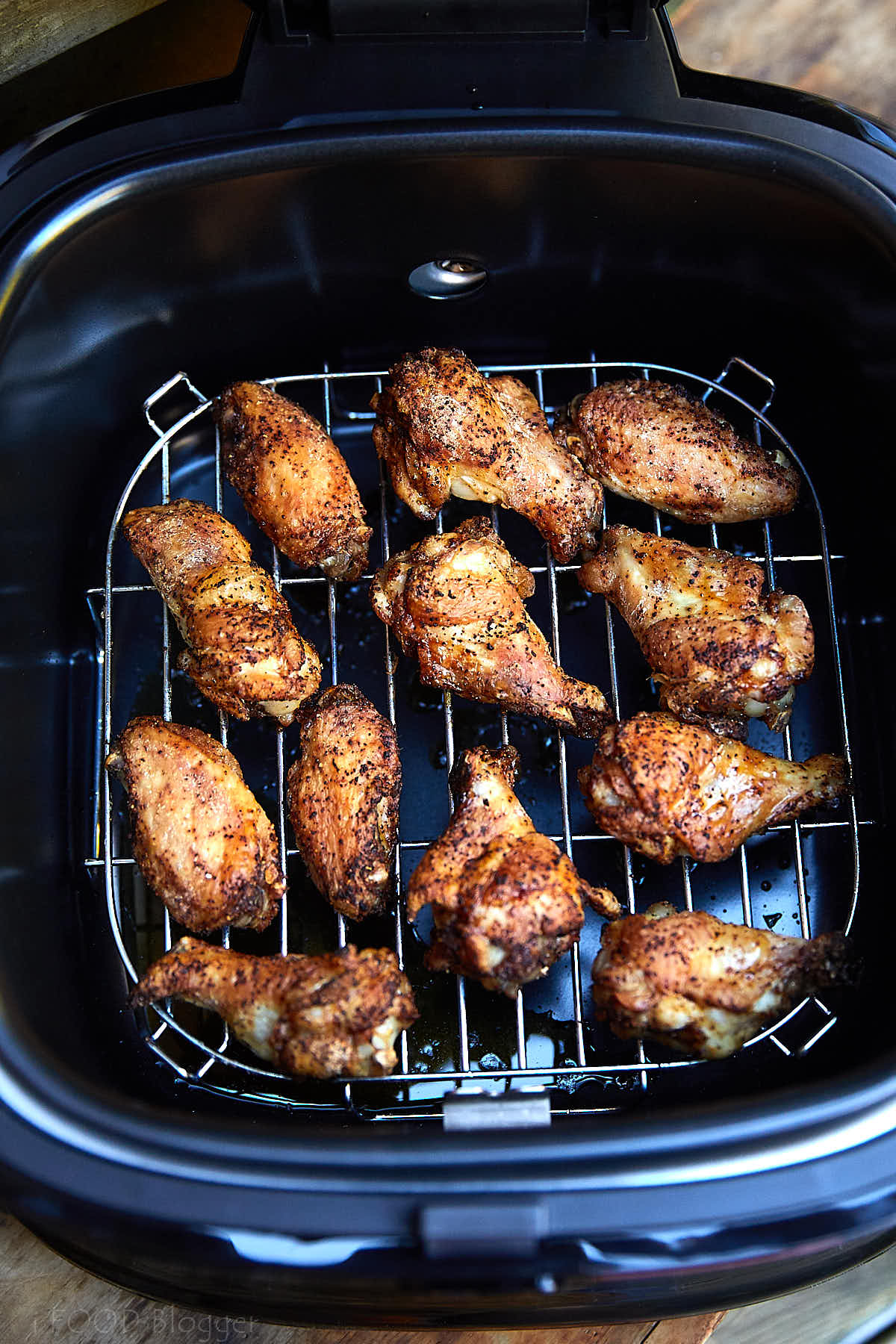 Crispy browned chicken wings inside an open air fryer.