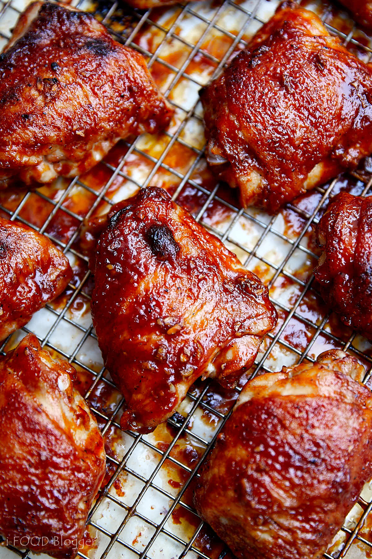 Well-browned chicken thighs glazed with BBQ sauce on a cooling rack over a baking sheet.