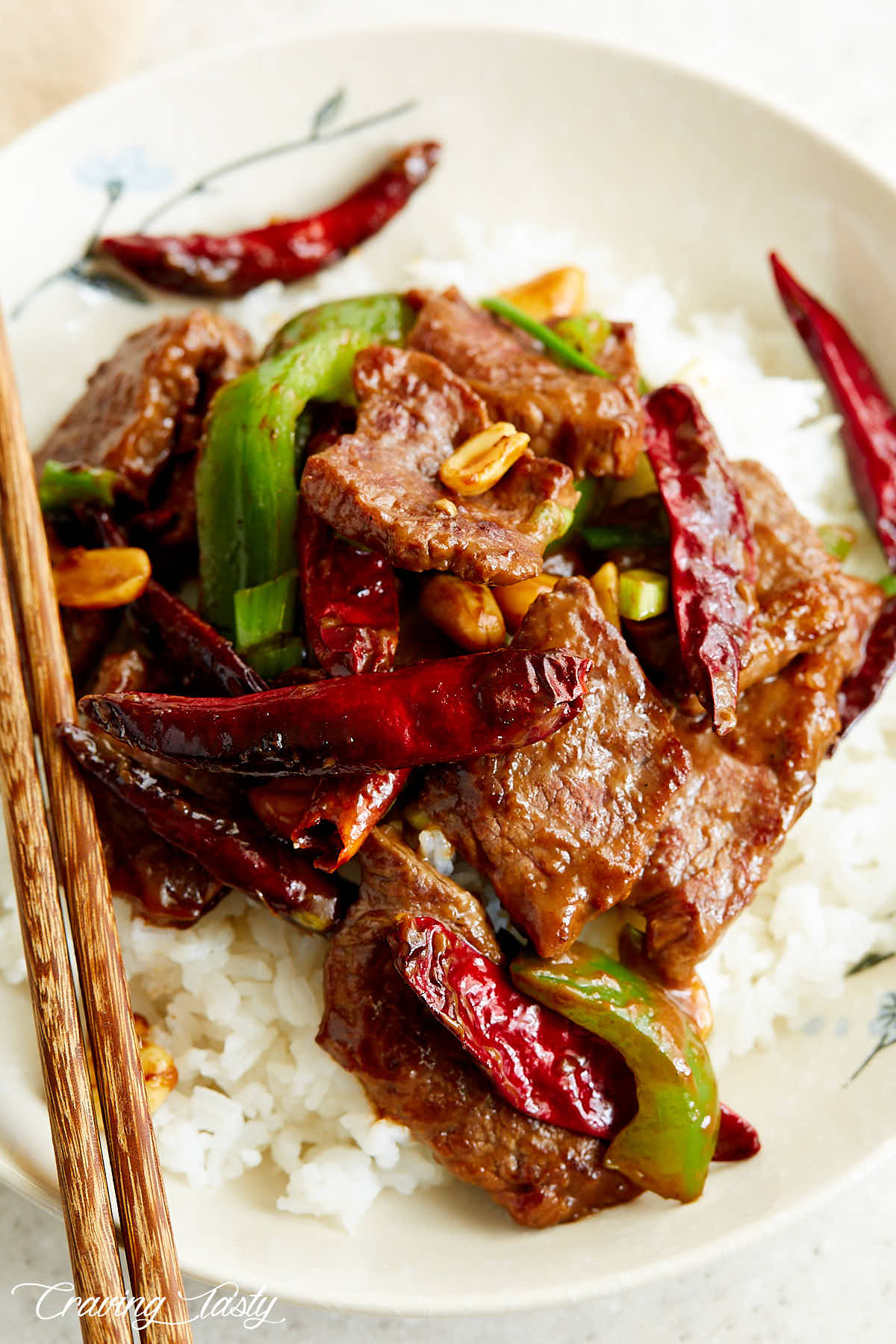 Kung pao beef in a white bowl over white rice with chopsticks on the side.