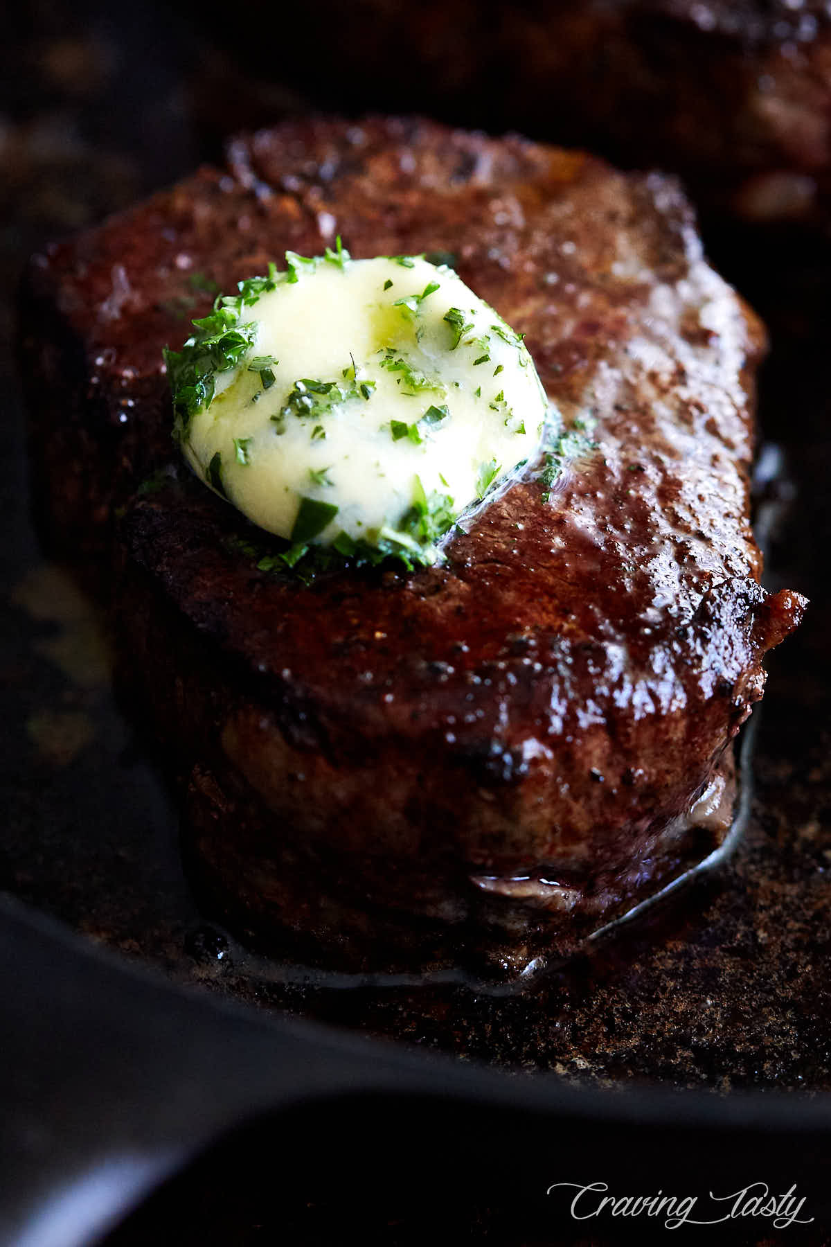 Close up of a juicy filet mignon steak topped with melting herb butter.