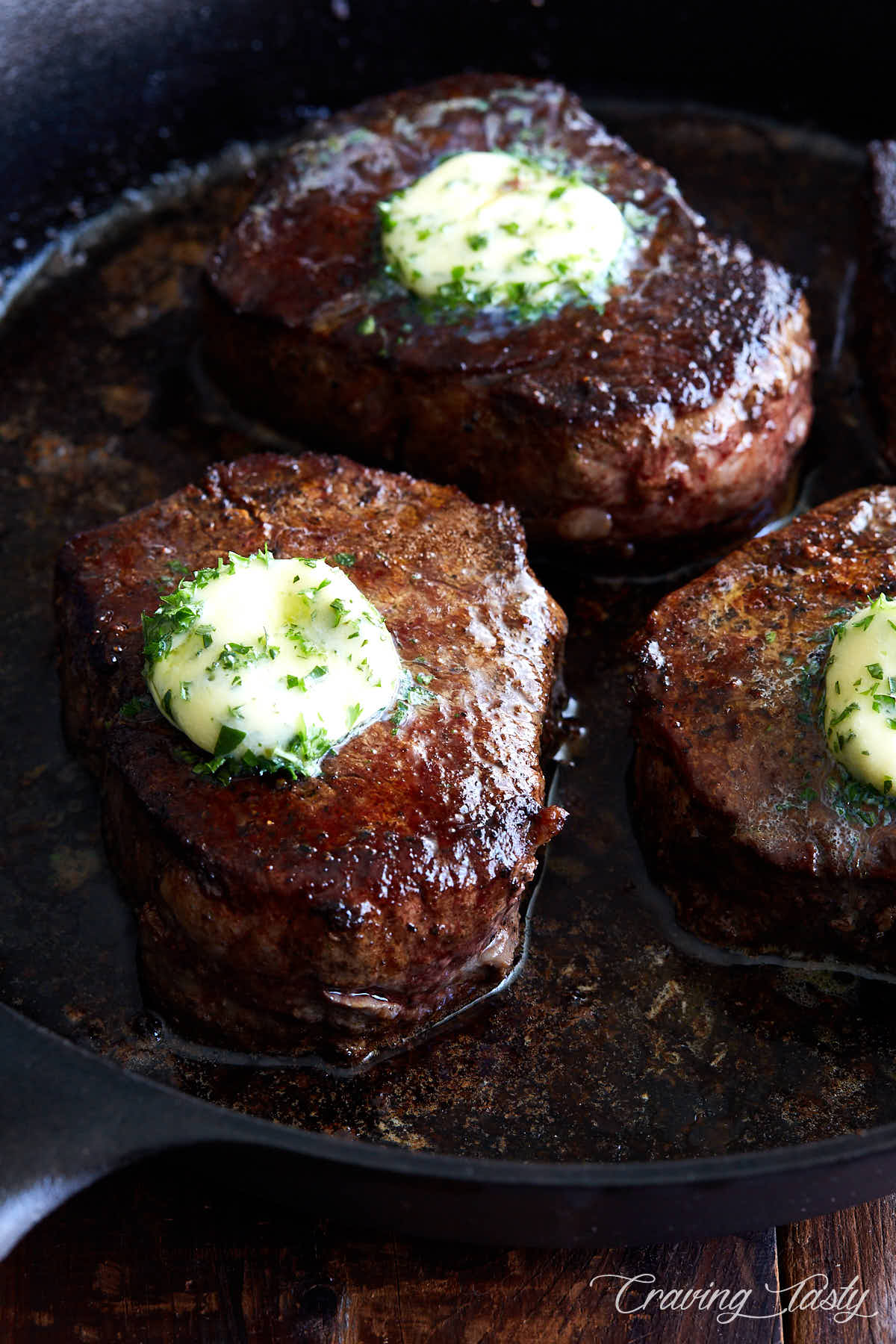 Filet mignon steaks in a cast iron pan topped with melting herb butter.