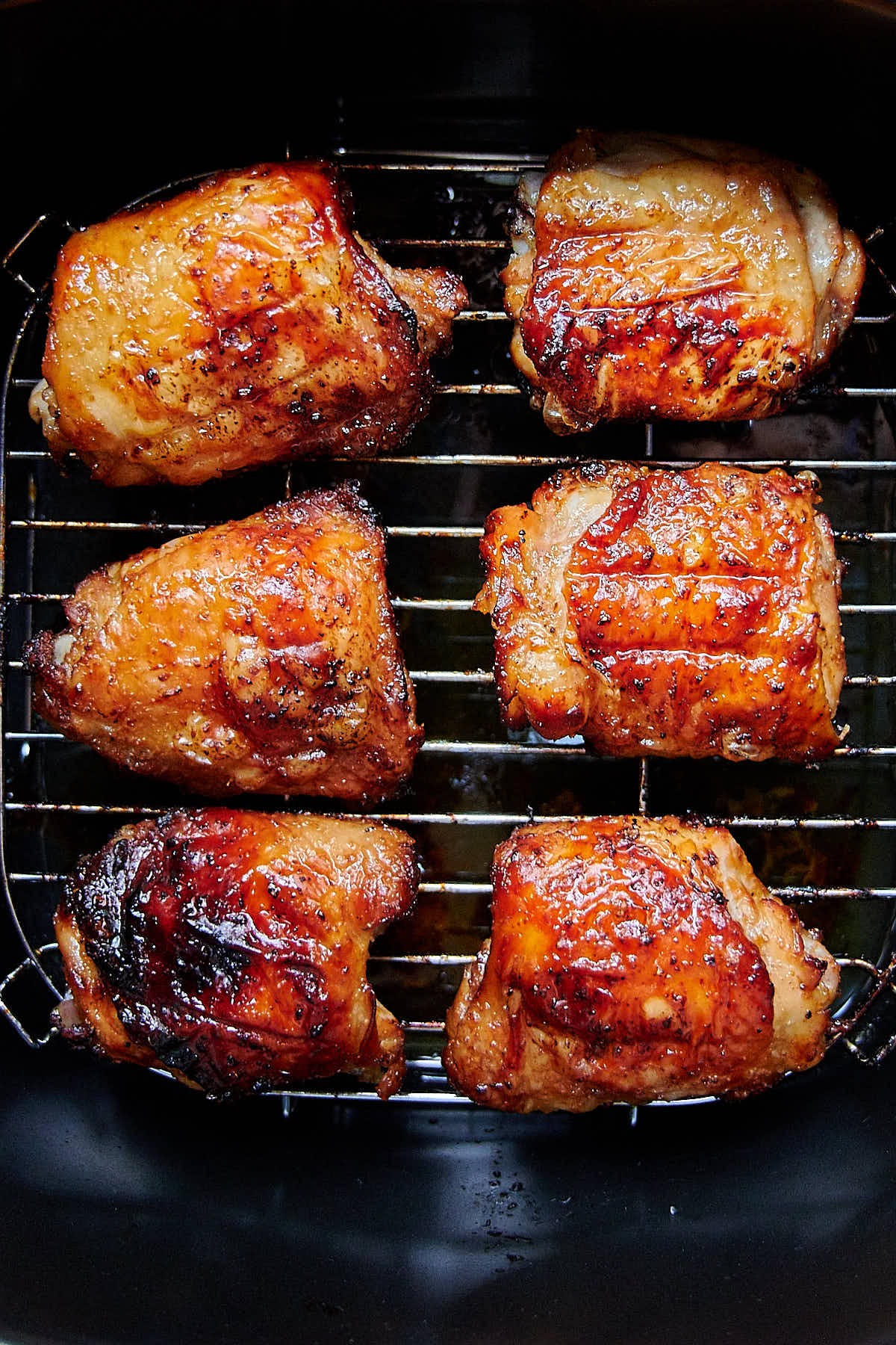 Top down view of six golden-brown, crispy chicken thighs inside an air fryer.