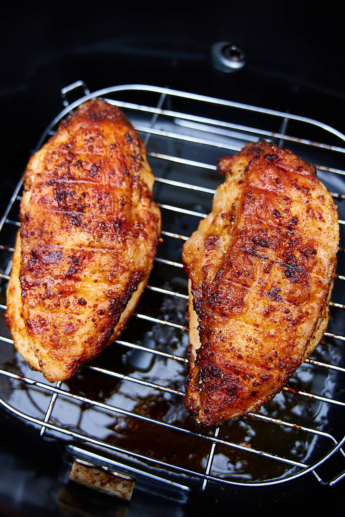 Two crispy, golden brown air fried chicken breasts sitting on a rack inside an air fryer.