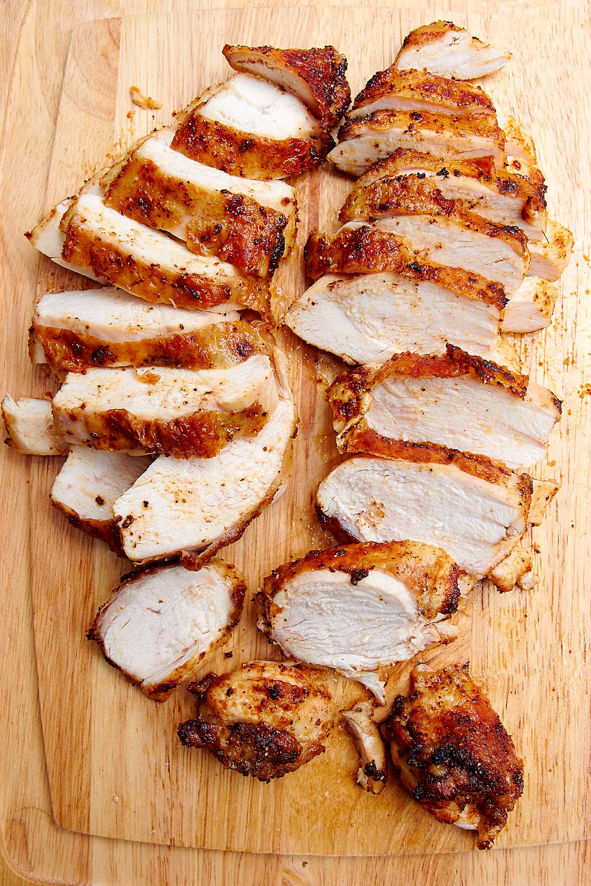 Air fried chicken breasts sliced into pieces on a bamboo cutting board, juices running off.