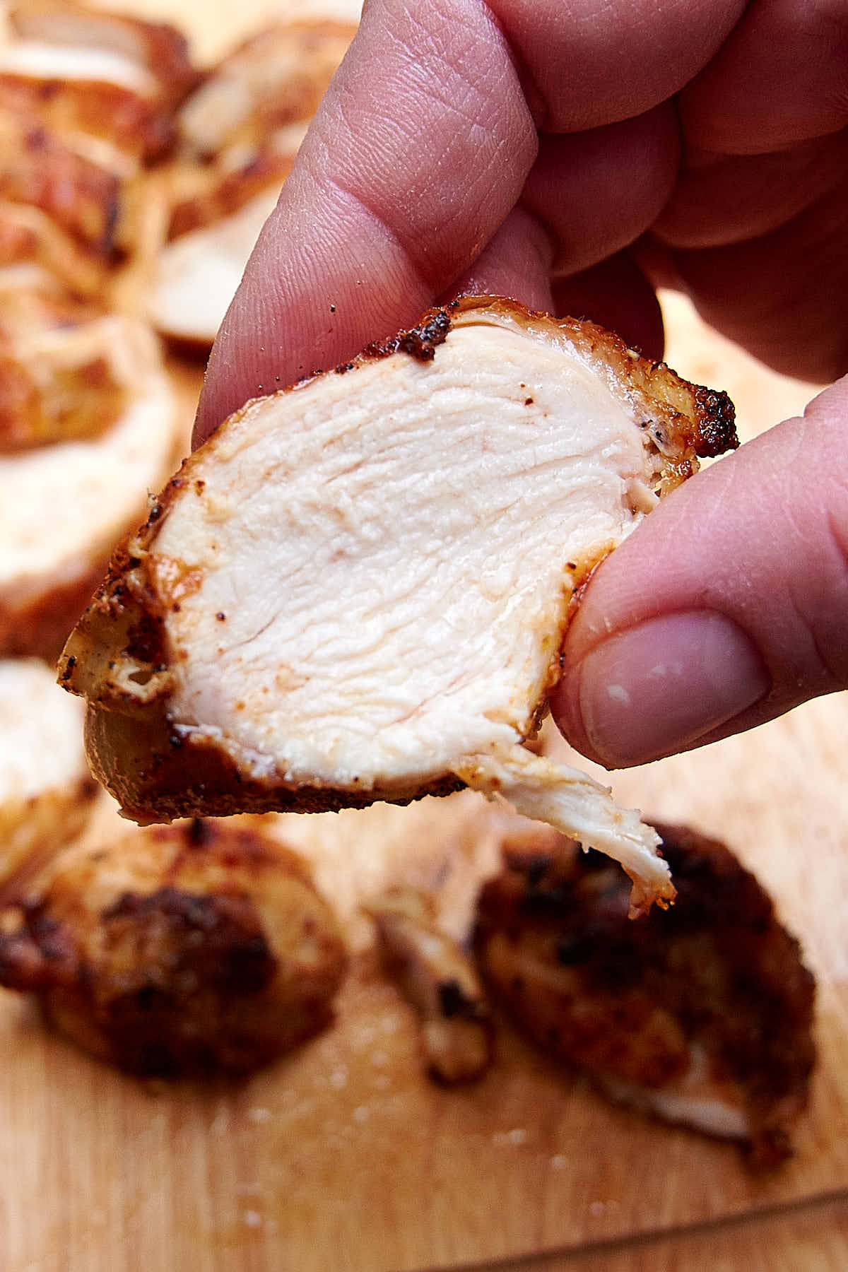 A slice of an air-fried chicken breast help by fingers, show how juicy and most it is.