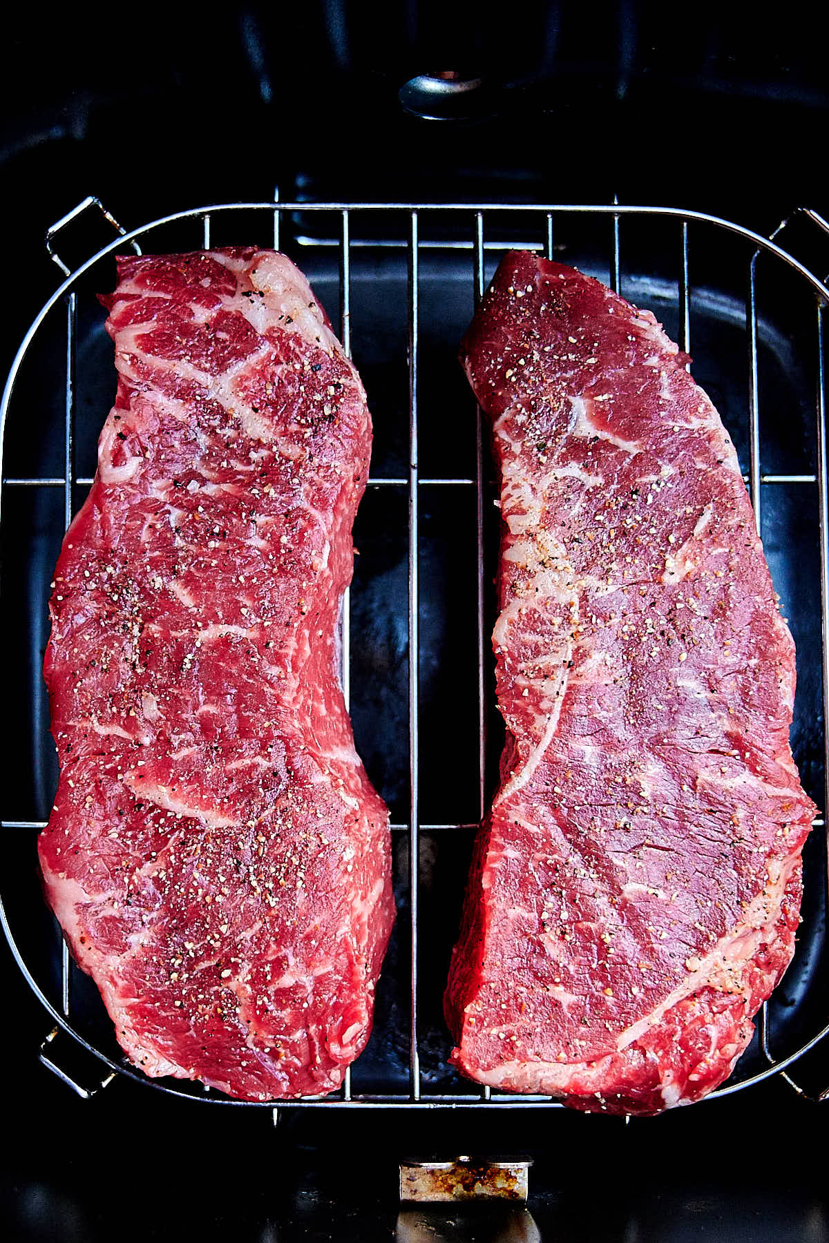 Two marbled raw steaks on a rack of an air fryer.