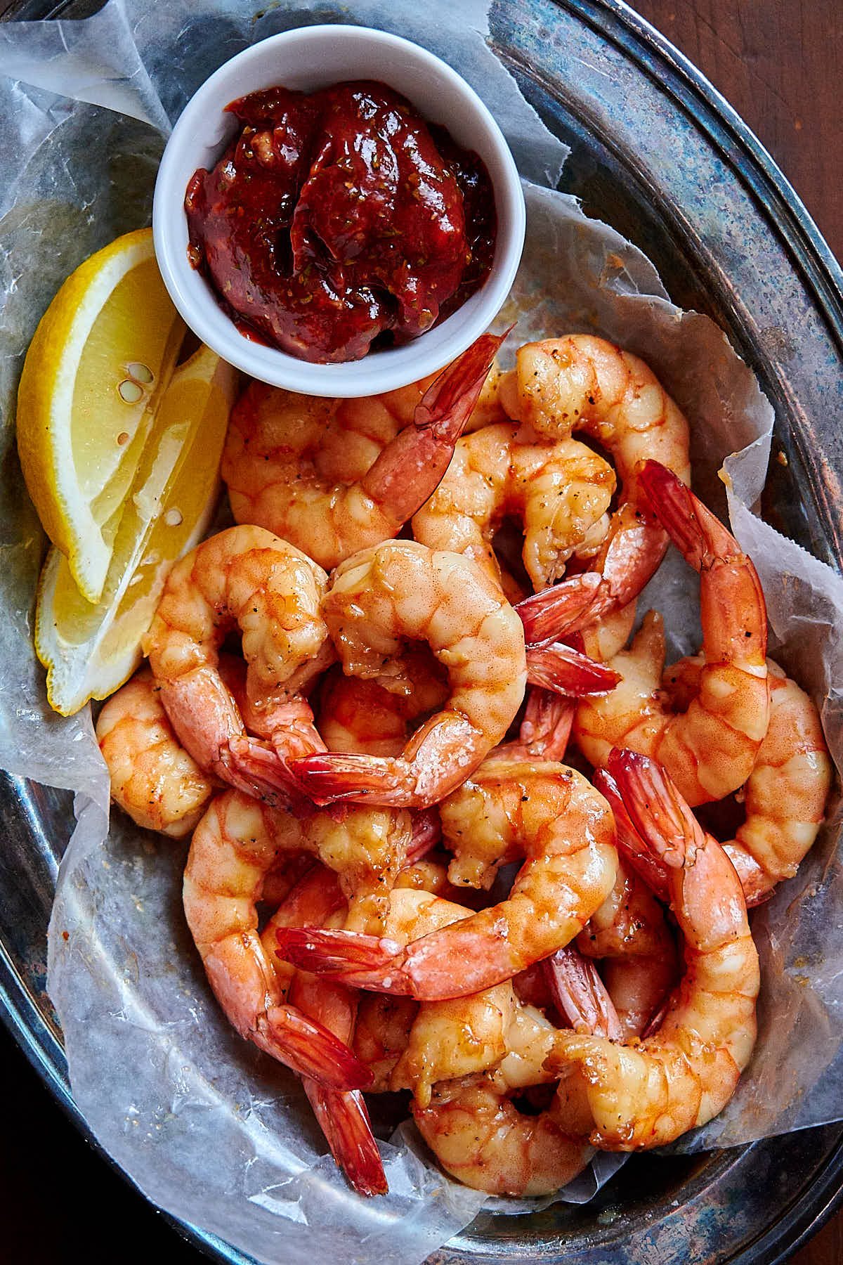 Air fried shrimp in a basket lined with white wax paper, with a lemon wedge a saucer with sauce on the side.