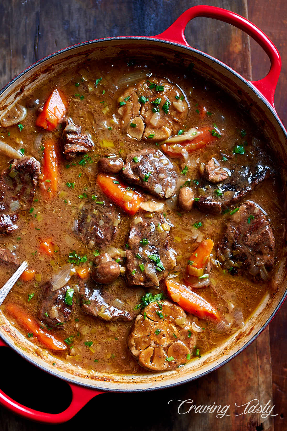 Braised beef with veggies and gravy in a red braising pan.