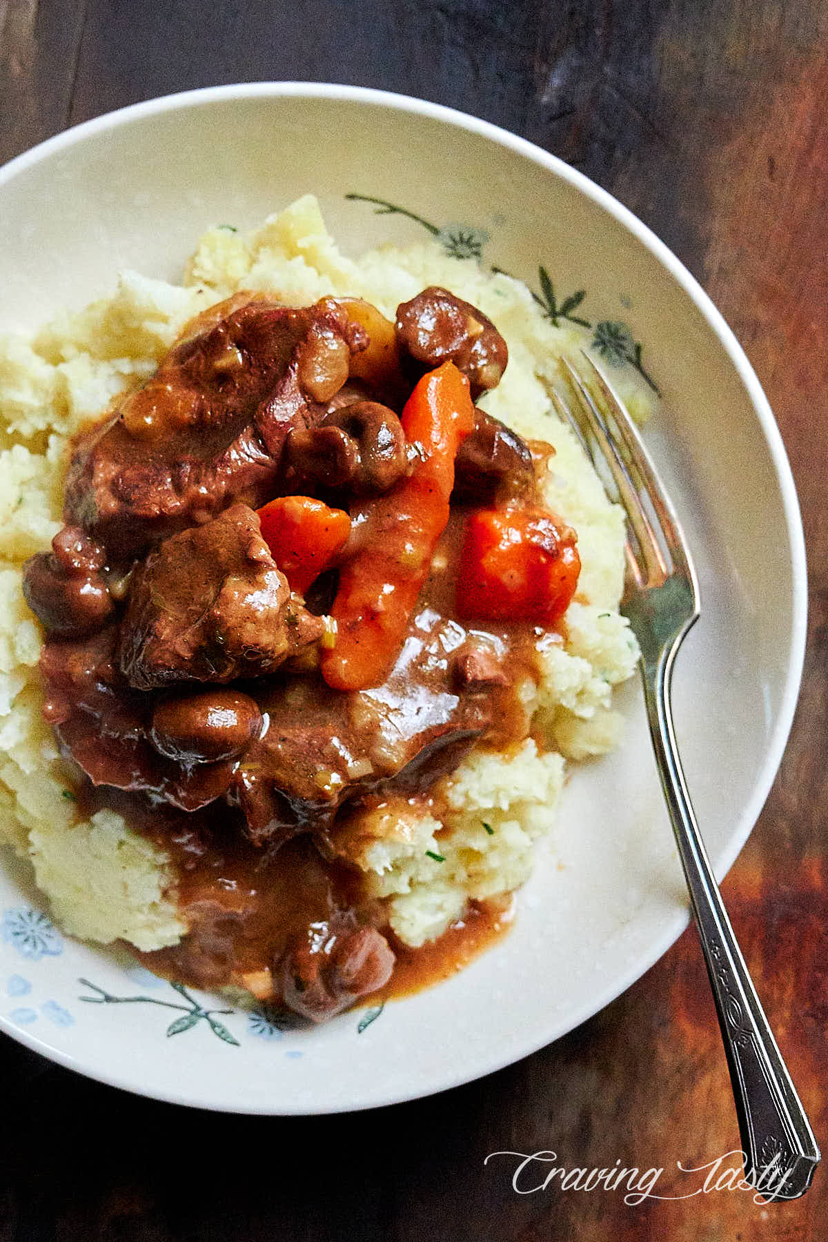 Braised beef over mashed potatoes in a white bowl.
