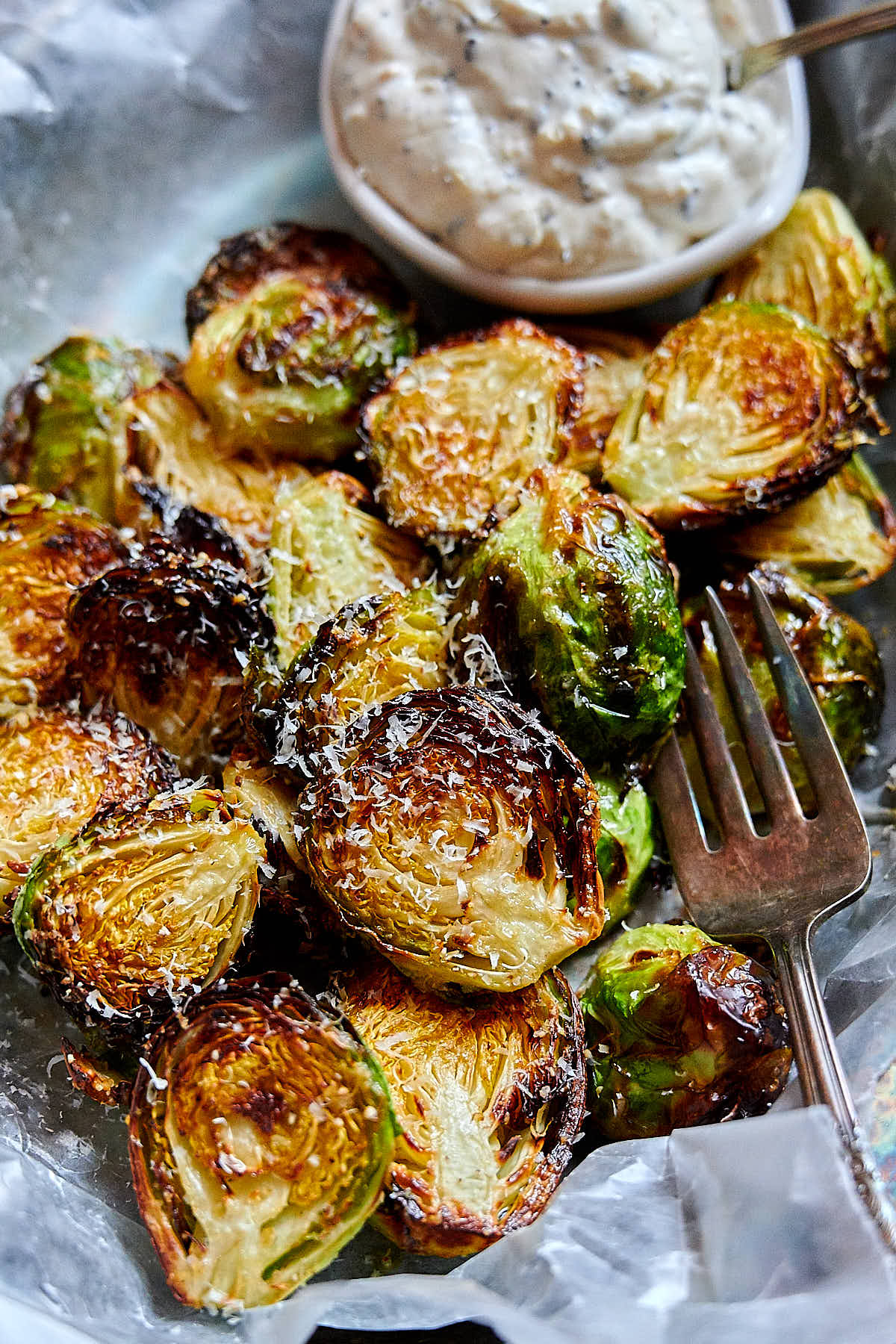 Crispy air fried Brussels sprouts, seasoned with olive oil, Parmesan cheese, salt and pepper in a serving basket with white sauce on the side.