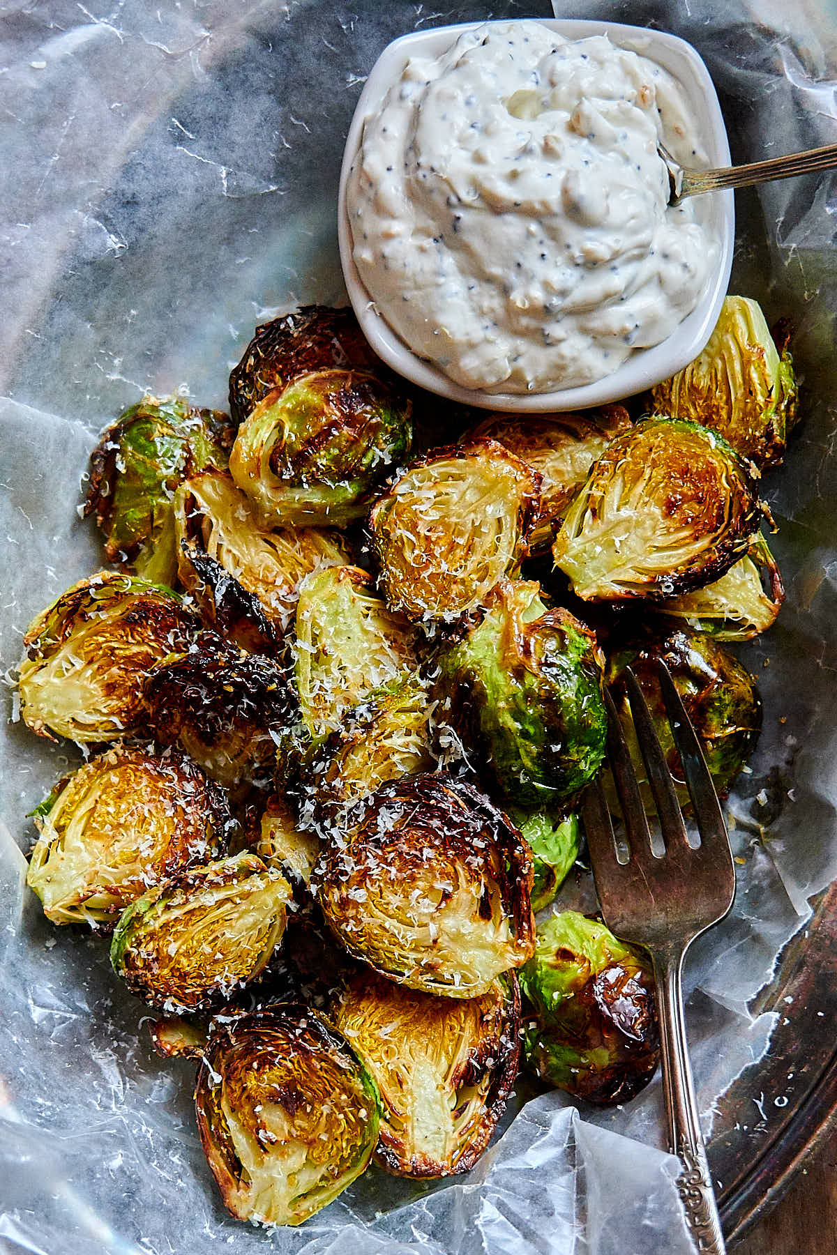 A close up of crispy, browned Brussels sprouts with a saucer full of dipping sauce and a fork on the side.