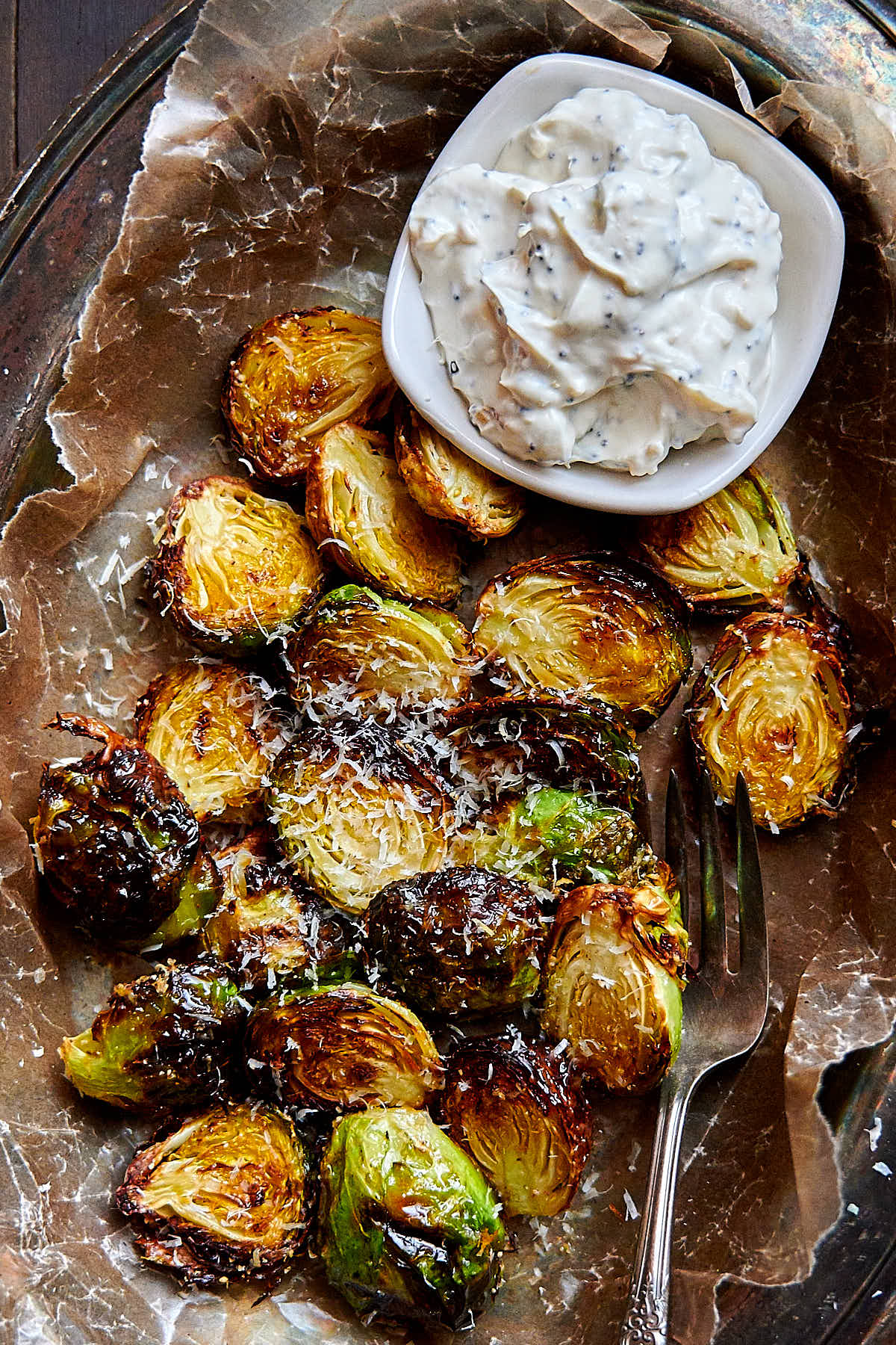 Top down view of crispy air fried Brussels sprouts and a white dipping sauce in a saucer on the side.