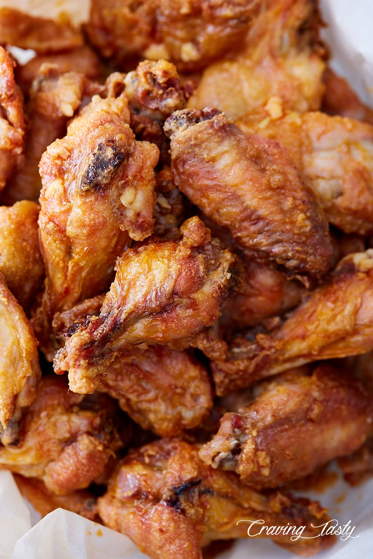 A big pile of crispy baked chicken wing on white parchment paper.