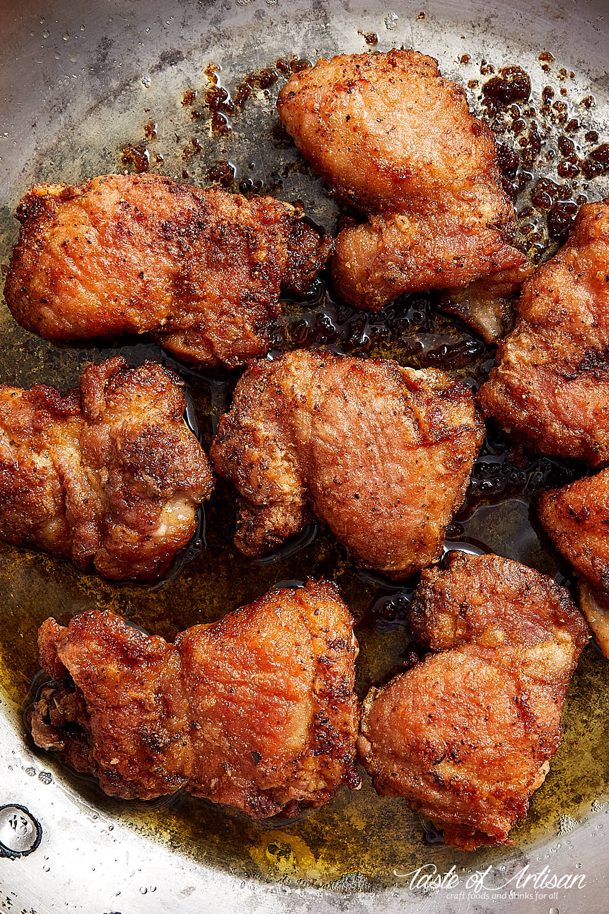 Pan-fried boneless skinless chicken thighs on a pan with oil.