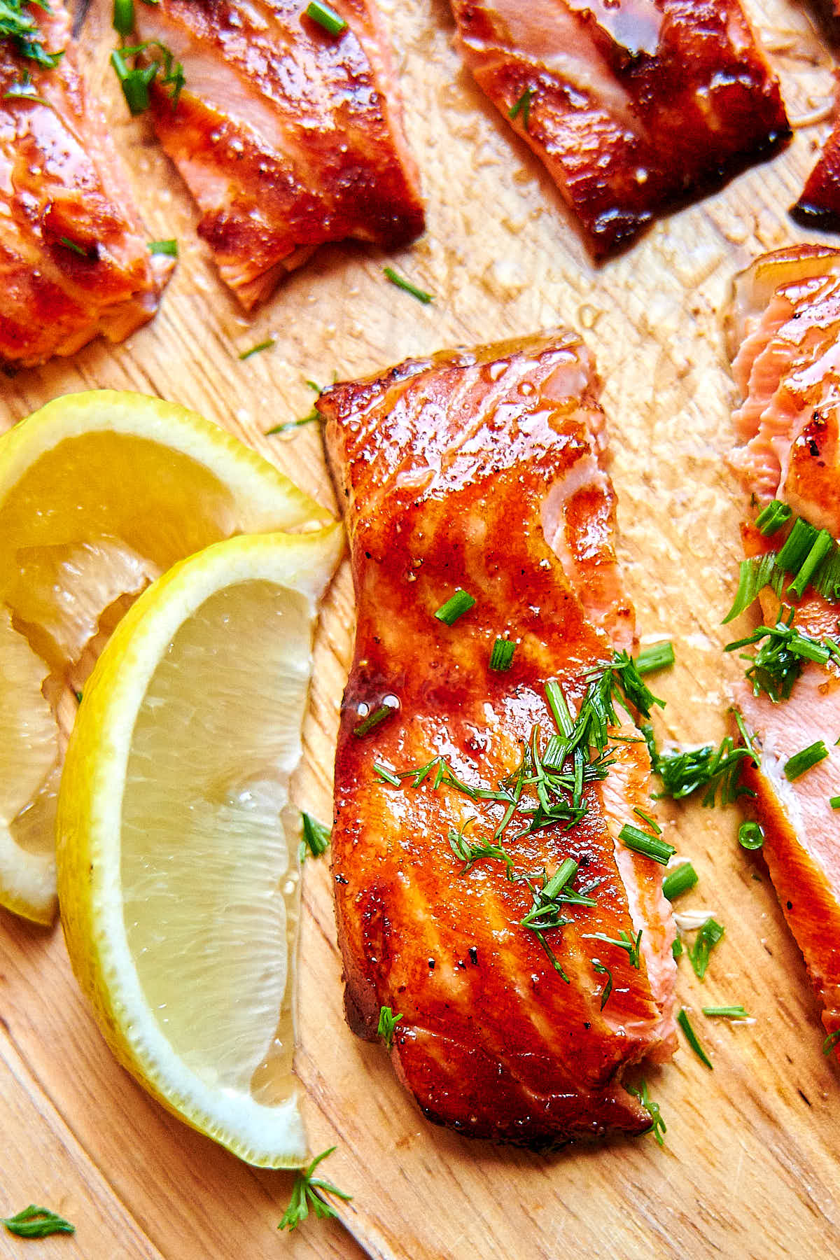 Close up of air fried salmon filet pieces with chopped dill on top, with lemon wedges on the side, on a cutting board.