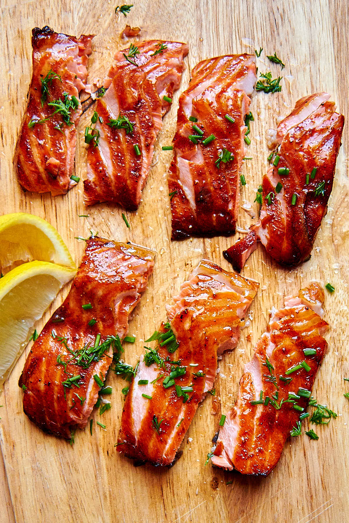 Air fried salmon filet pieces on a cutting board with lemon wedges on the side.