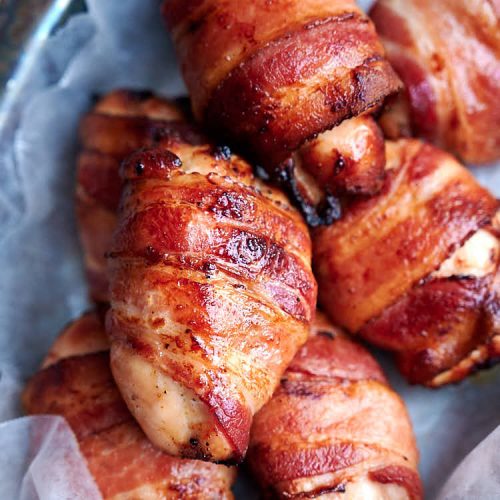 Chicken thighs wrapped in bacon, cooked, in basket lined with white wax paper.